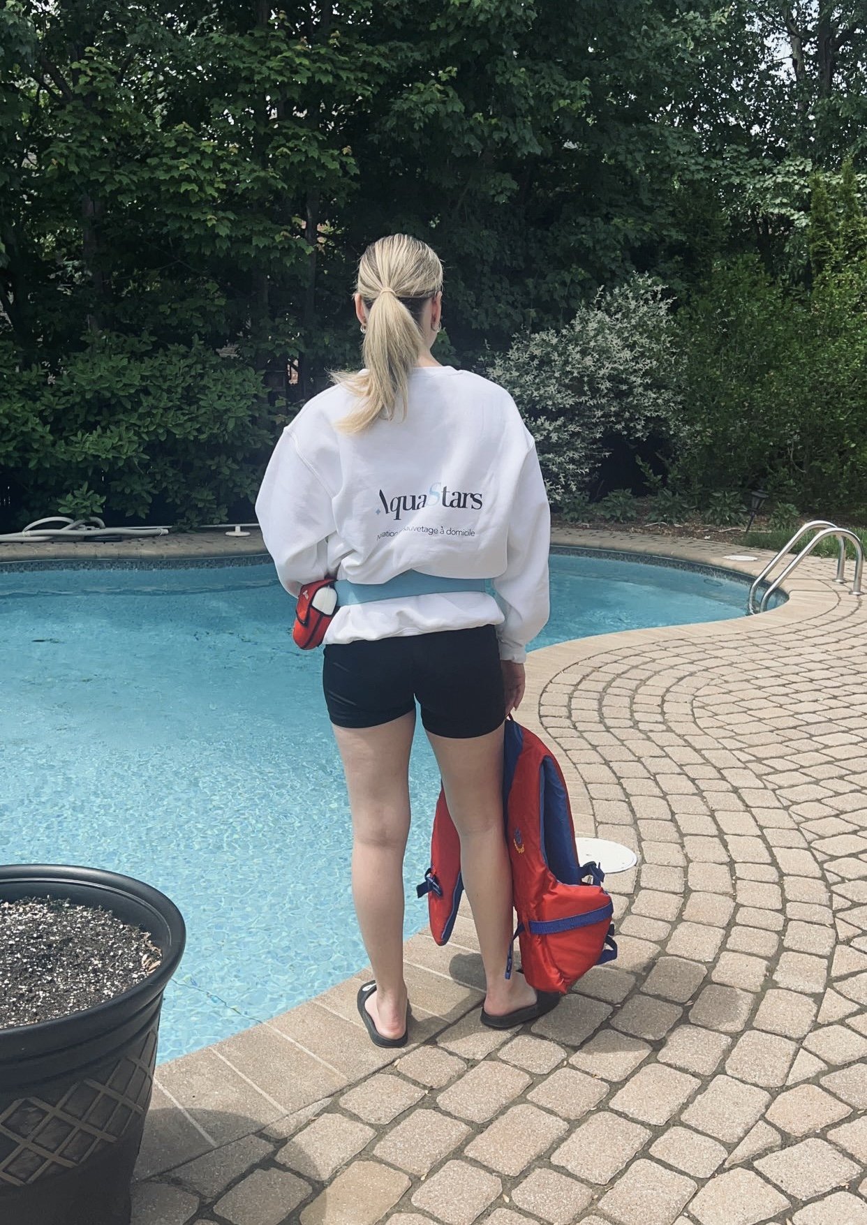 Une monitrice pose devant une piscine avec un chandail personnalisé au logo d'AquaStars, école de natation à domicile
